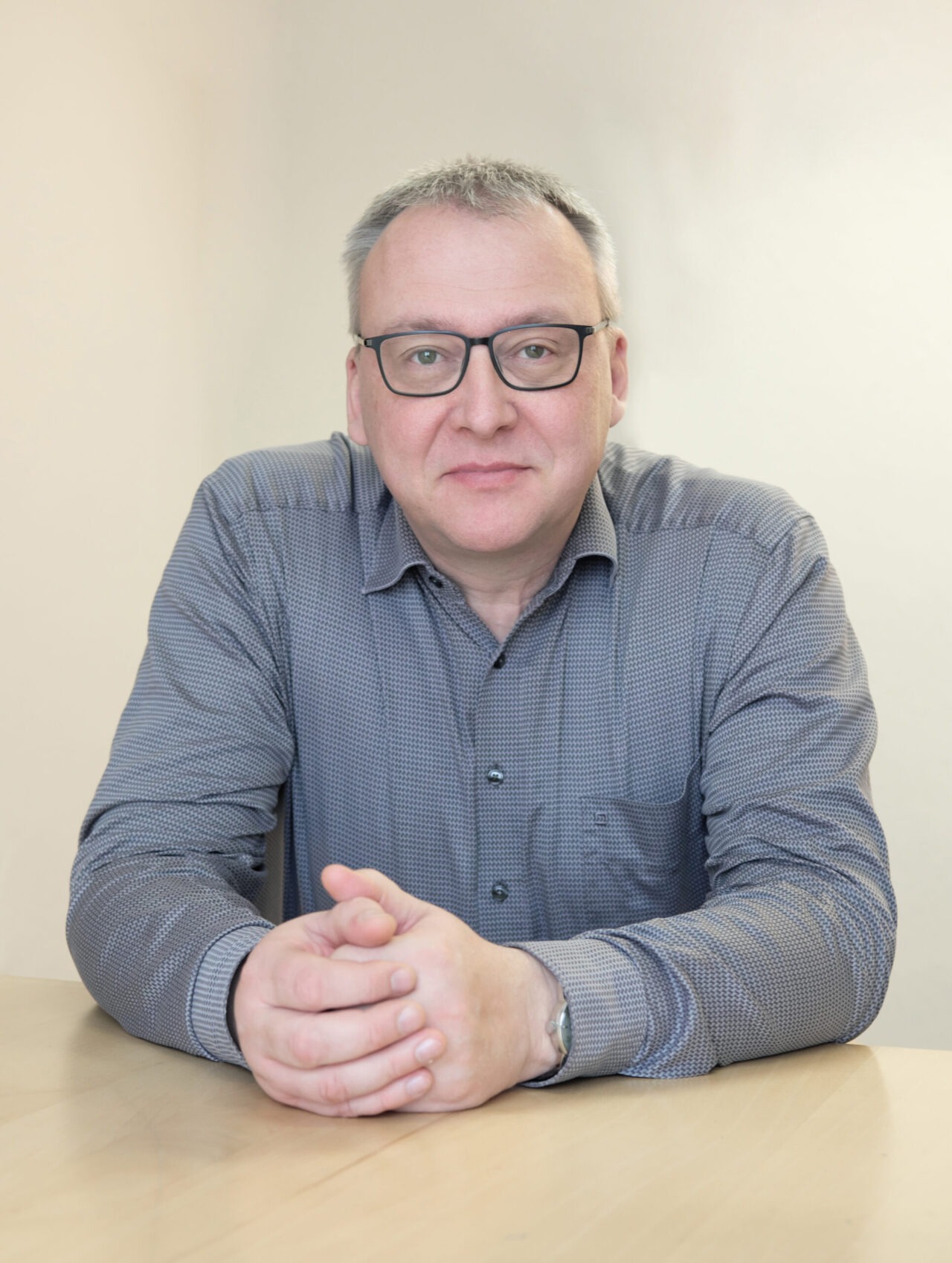 Mann sitzt am Tisch, Hände gefaltet.