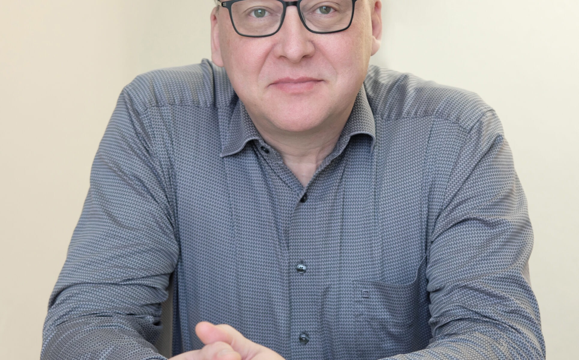 Mann sitzt am Tisch, Hände gefaltet.